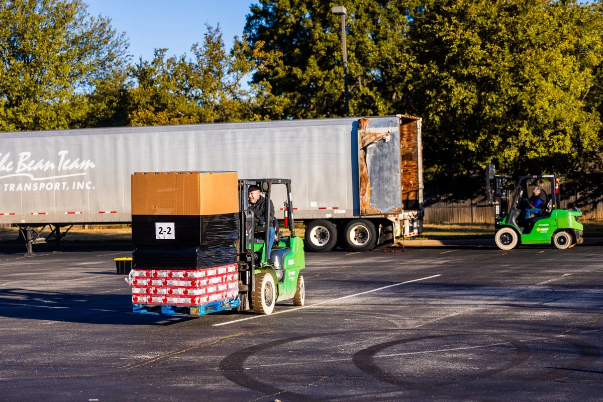 Forklift operators handling palletized goods beside a freight trailer.